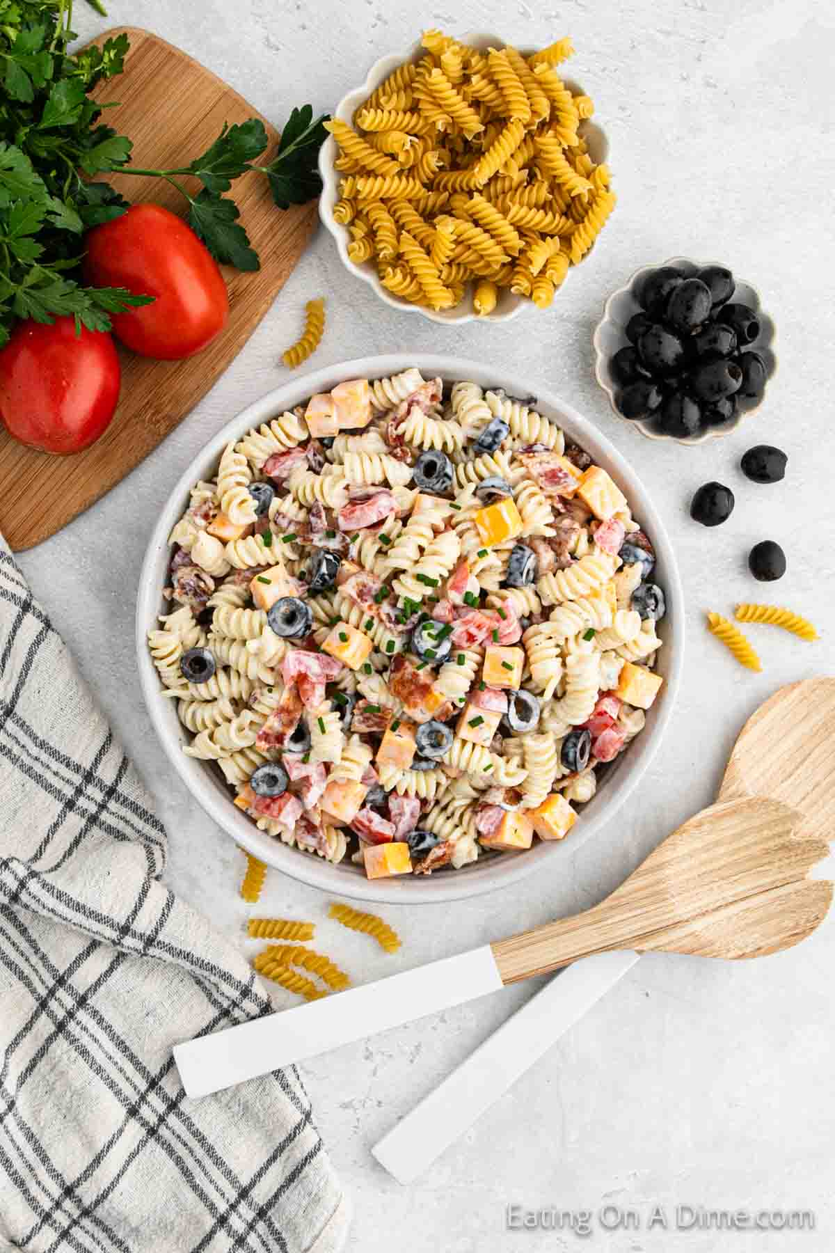Bacon ranch pasta salad in a bowl with a bowl of black olives, pasta and tomatoes on the side