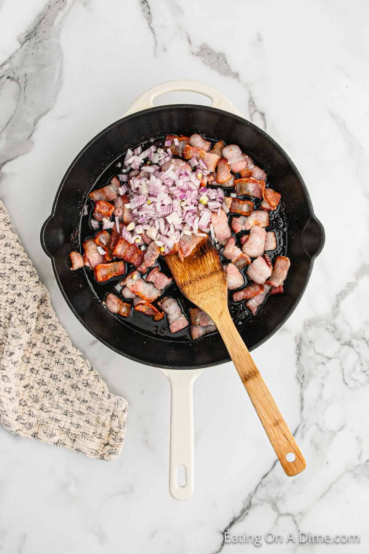 Mixing in red onions in a skillet with the bacon