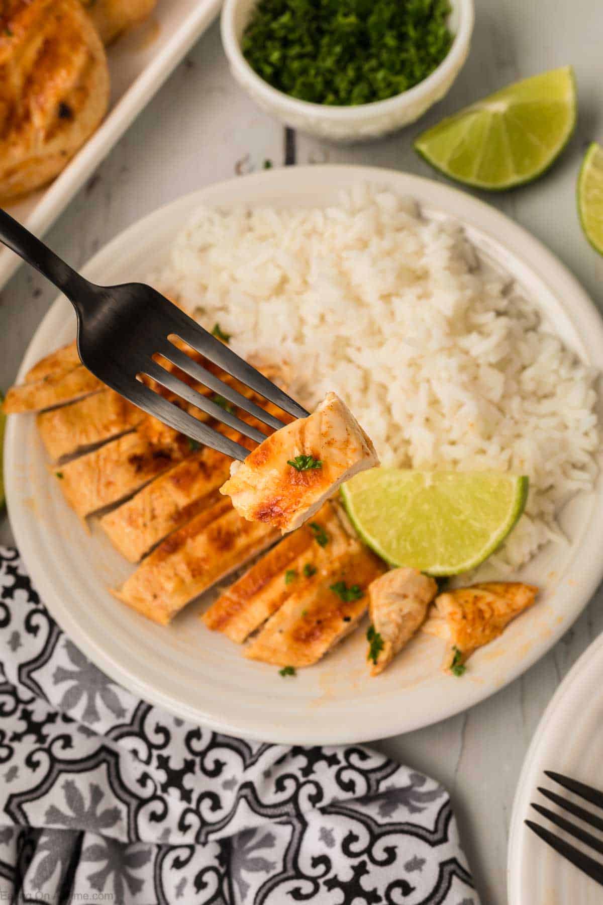 Chicken breast sliced on a plate with a bite on a fork and white rice on the plate