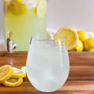 A small glass of lemonade with a lemon slice on the edge of it.