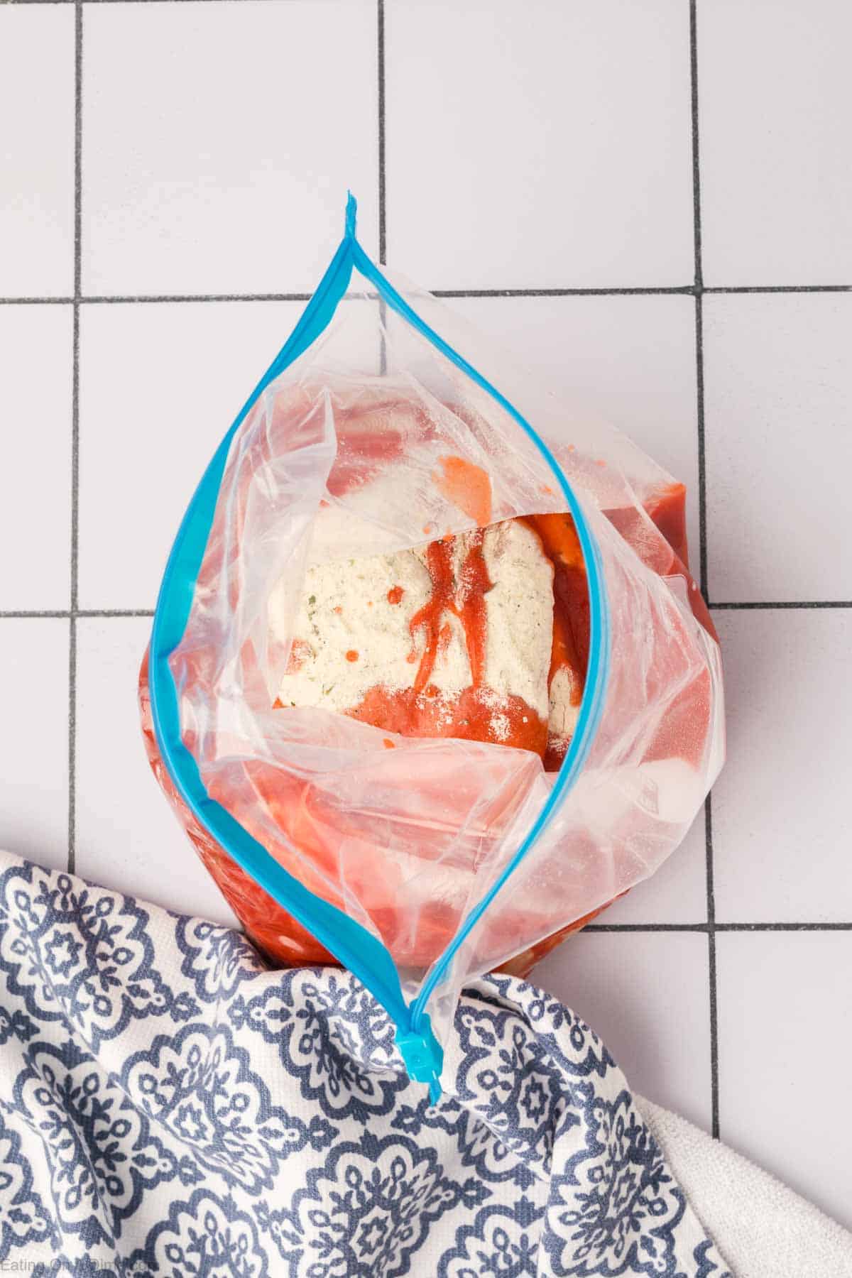 Chicken placed in a zip lock bag and topped with buffalo sauce and ranch dressing mix