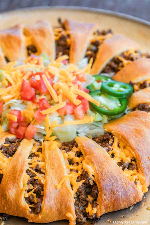 Close up Taco Crescent Roll Ring topped with lettuce, tomato, shredded cheese and jalapeños. 
