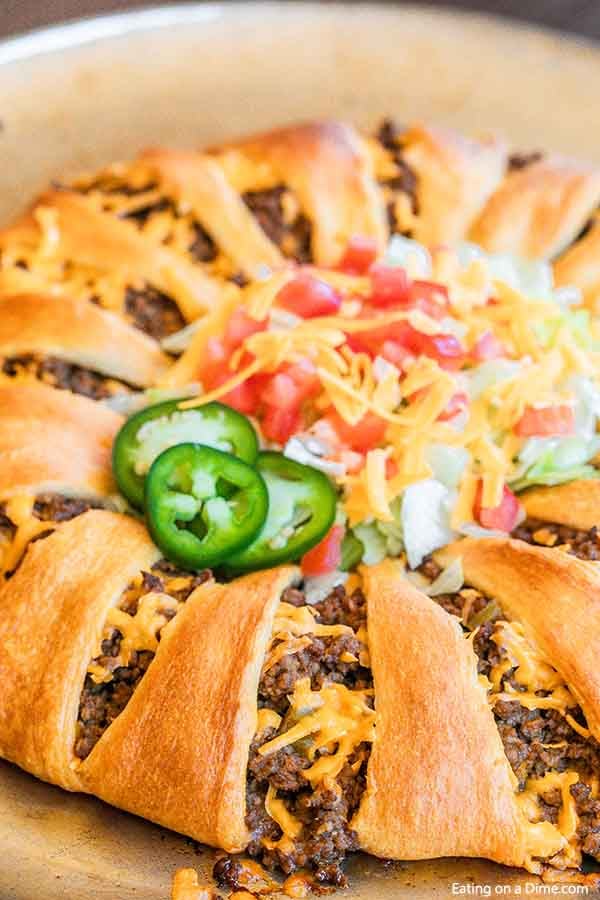 Taco Crescent Roll Ring topped with lettuce, tomato, shredded cheese and jalapeños on a pizza pan. 