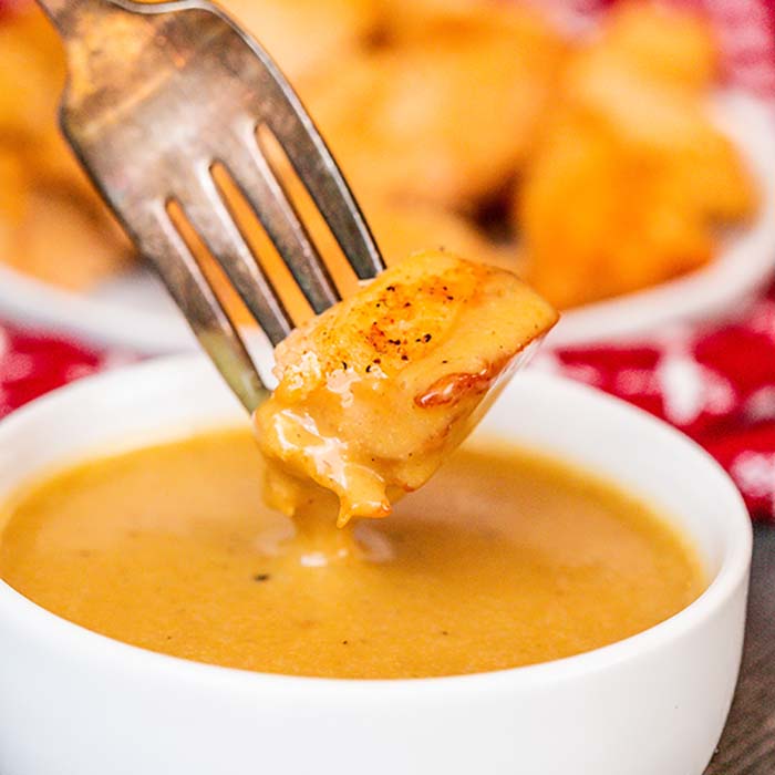 Close up image of chick fil a sauce in a white bowl being dipped with a chicken nugget on a fork. 