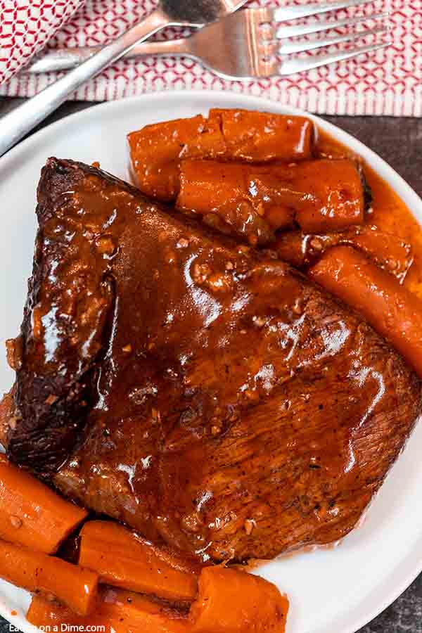 Close up image of beef brisket on a white plate with a side of cooked carrots. 