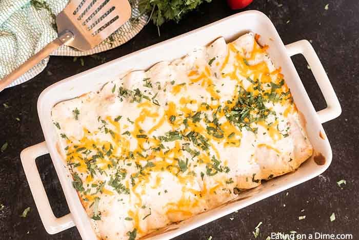 A pan full of green chili chicken enchiladas on a black latter with a spatula next to it 
