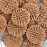 A close-up of several chocolate peanut butter cookies with a crisscross fork pattern on top, sprinkled with sugar, arranged in an overlapping pile on a cooling rack—perfect inspiration for your next chocolate peanut butter cookies recipe.