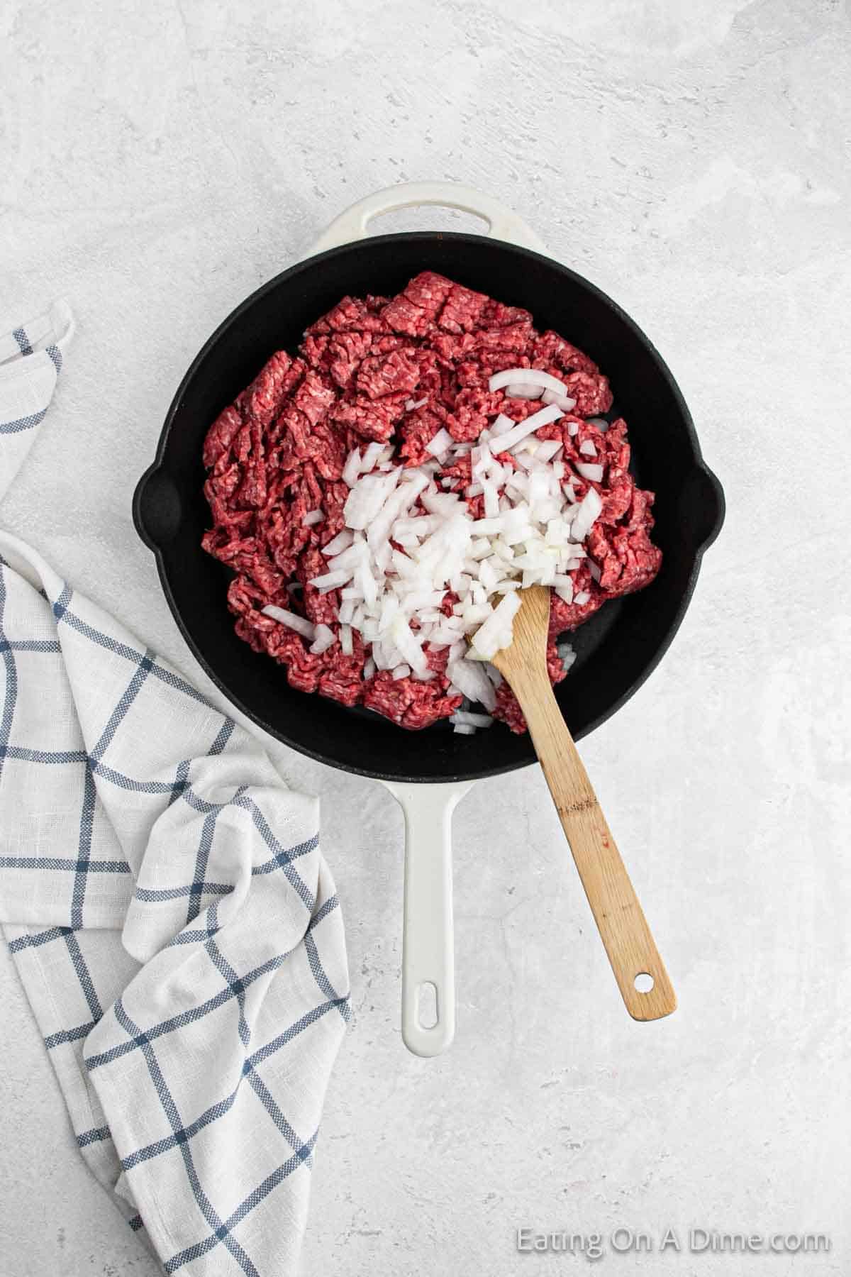 Cooked ground beef in a skillet with chopped onions and wooden spoon