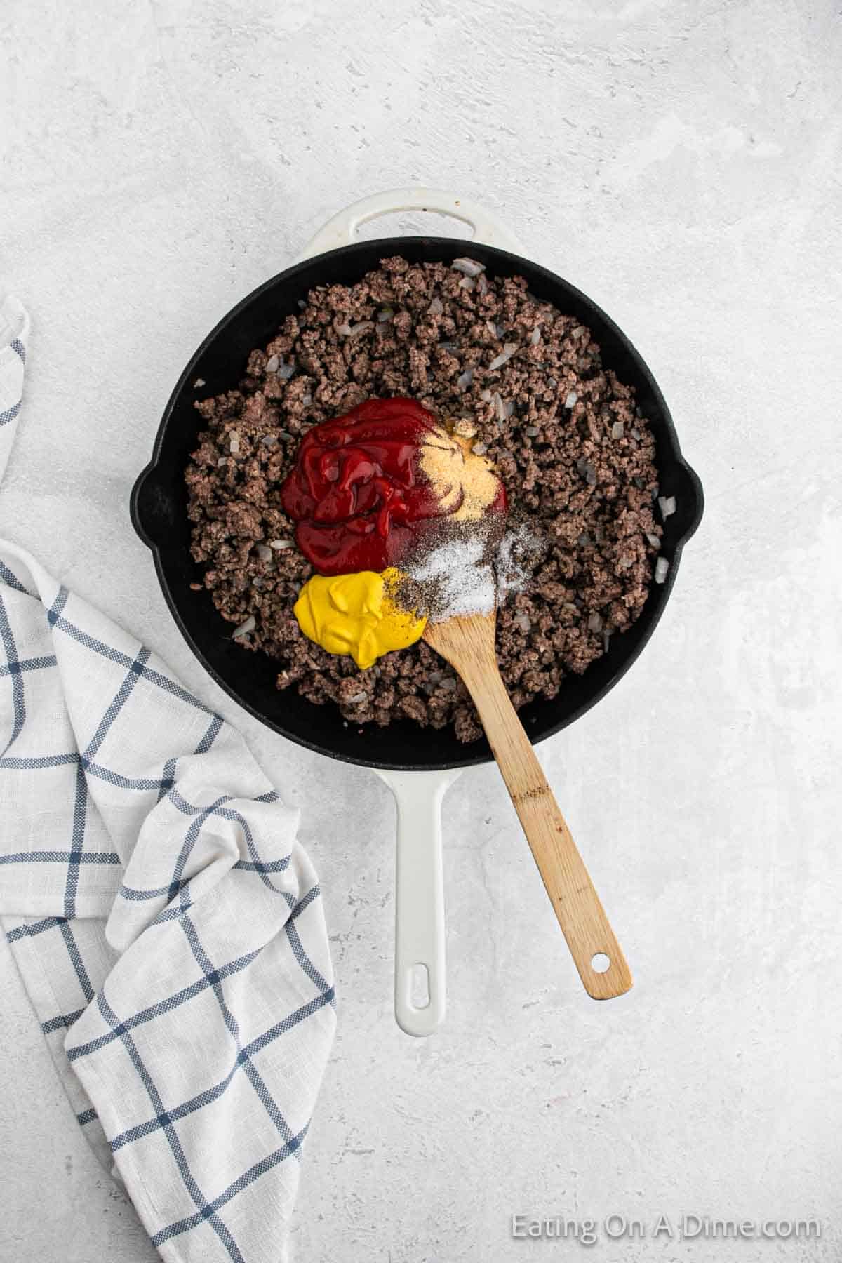 Cooked ground beef in a skillet topped with ketchup, mustard and seasoning