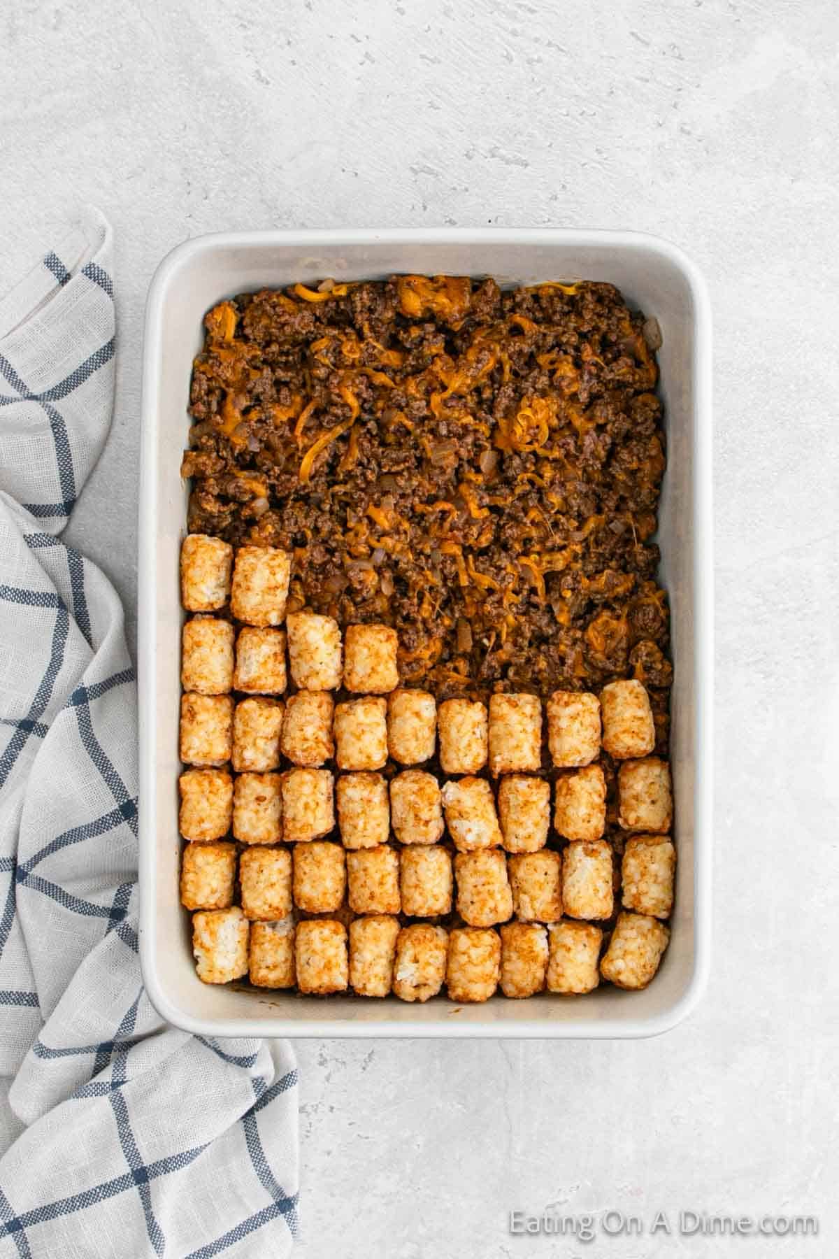 Layering ground beef mixture in a baking dish and topped with tator tots