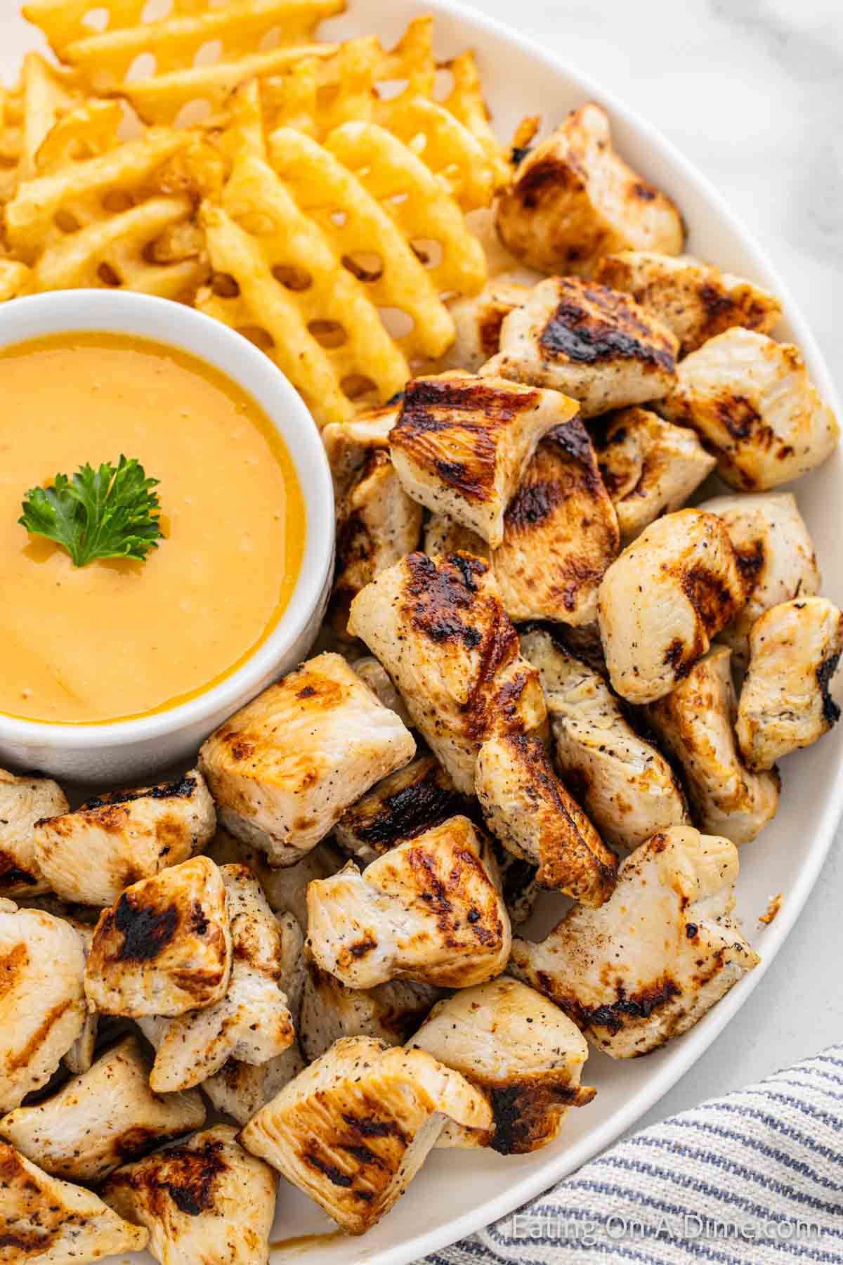 Grilled chicken nuggets on a platter with fries and dipping sauce