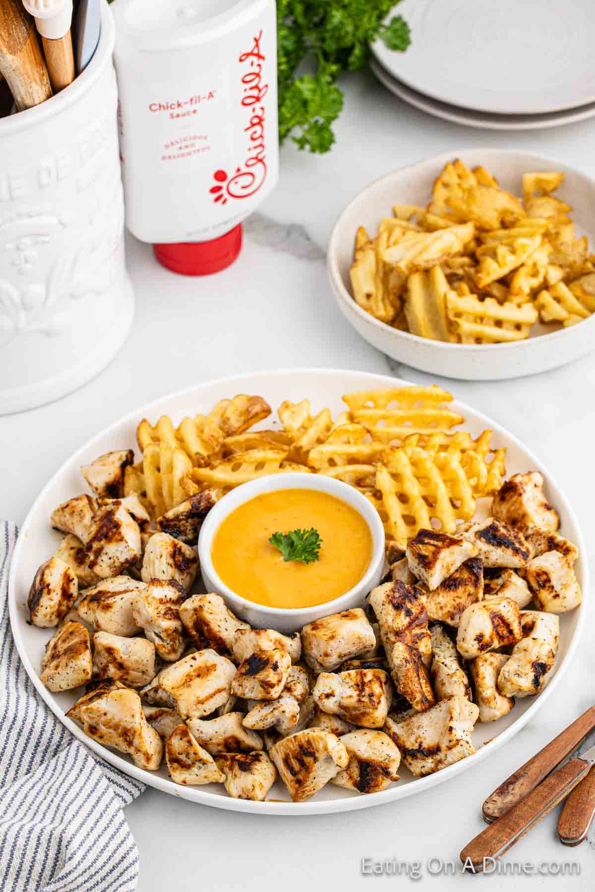 Grilled chicken nuggets on a platter with a side of fries and dipping sauce