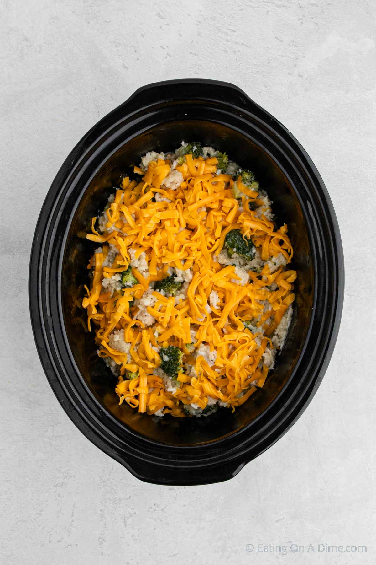 Topping the broccoli chicken mixture with cheese in the slow cooker