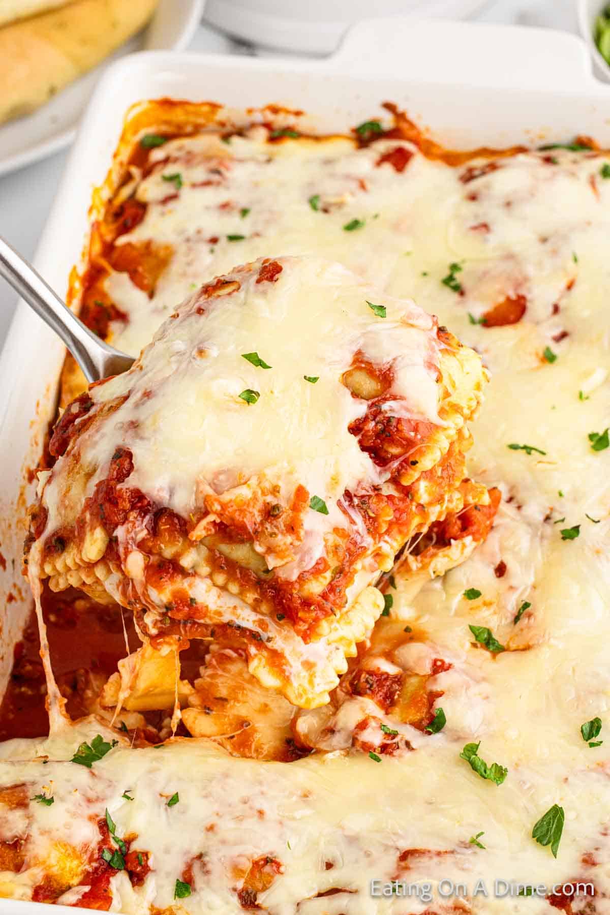 Close up image of baked ravioli in a casserole dish with a serving a serving spoon