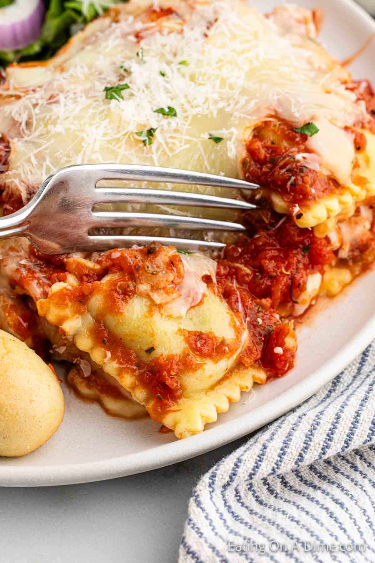 Close up image of Ravioli baked topped with sauce and melted cheese on a plate with a fork