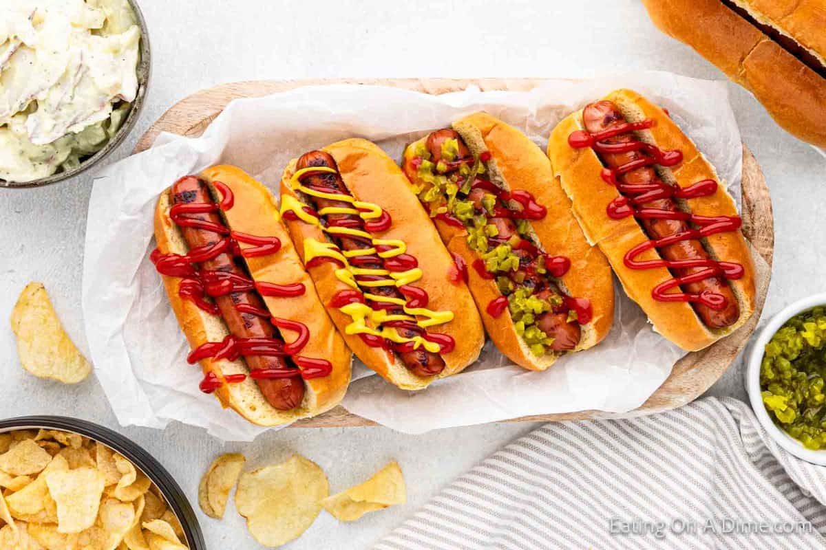 Grilled hot dogs on a platter topped with ketchup mustard and relish
