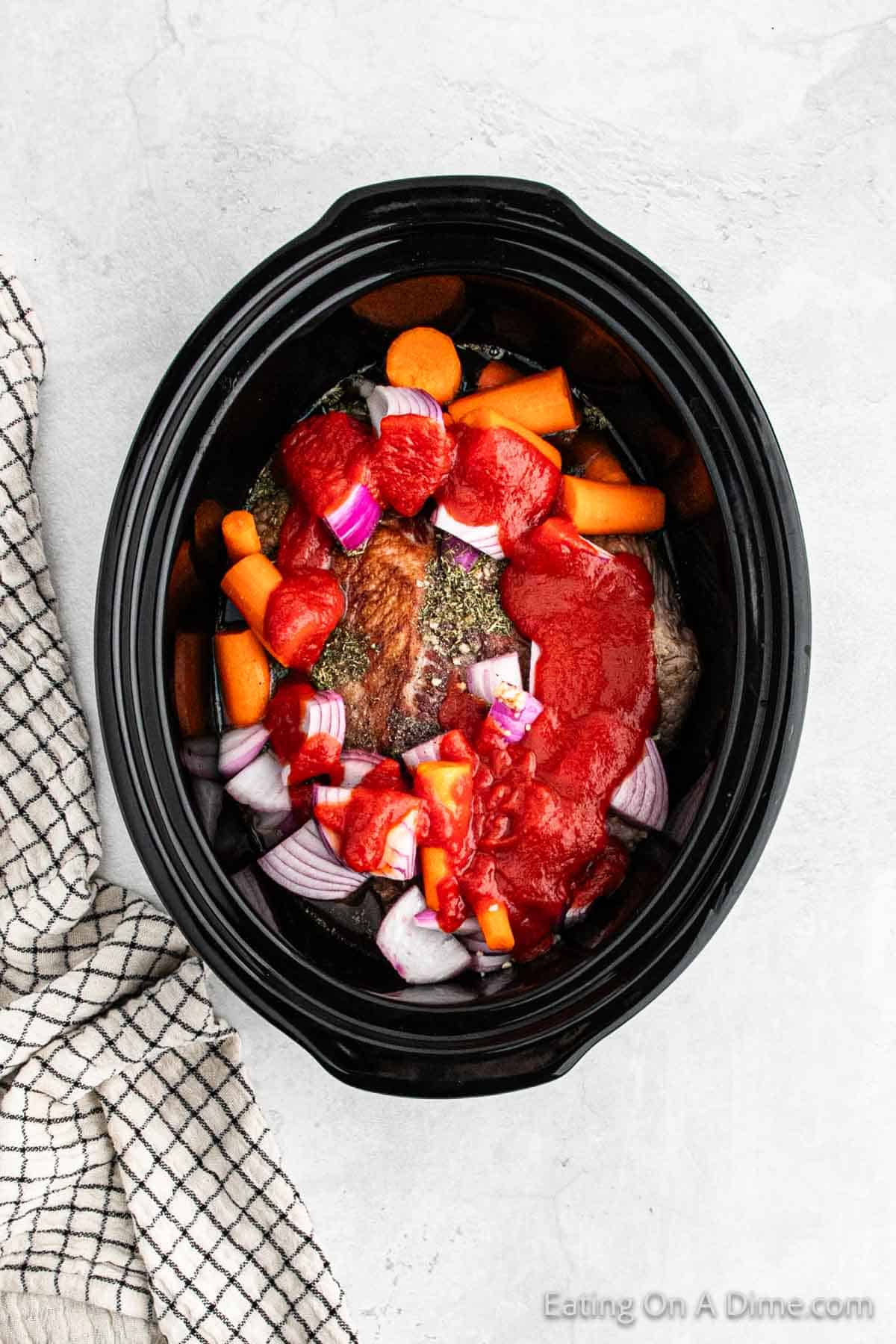 Topping carrots, red onion and brisket with seasoning and tomato sauce