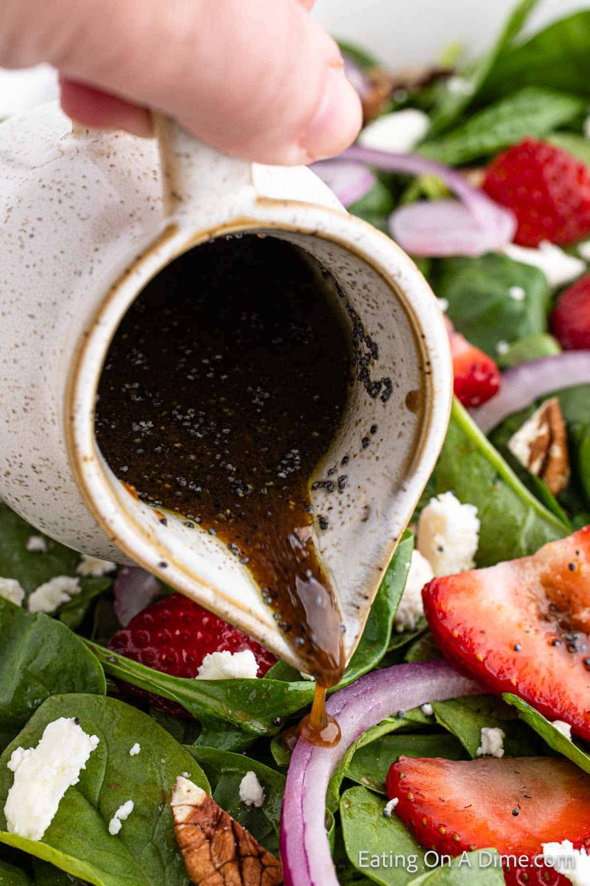 Pouring dressing over the top of the strawberry spinach salad