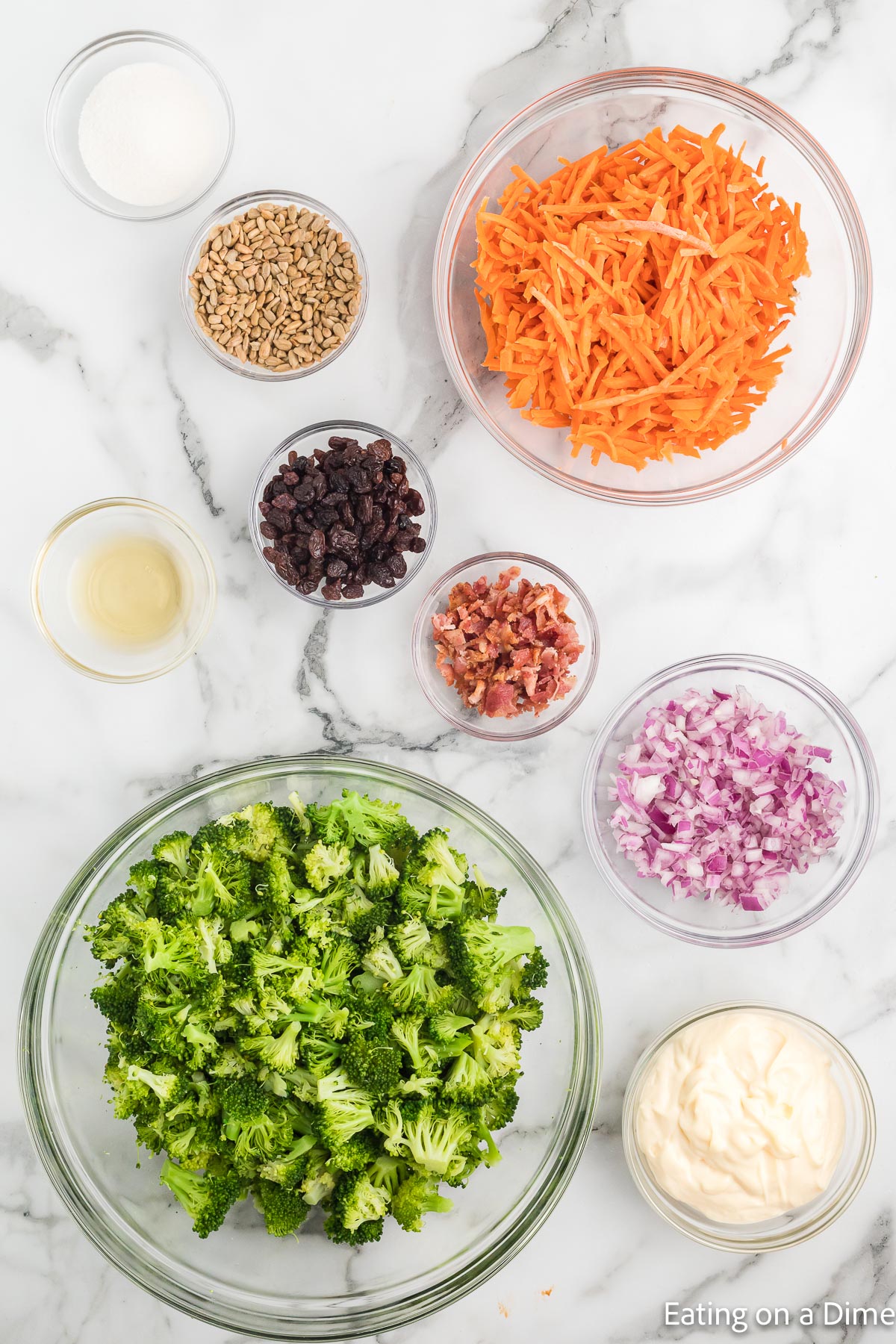 Ingredients needed for broccoli salad - broccoli florets, carrots, red onion, mayo, sugar, apple cider vinegar, raisins, bacon, sunflower seeds