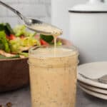 A spoon is pouring dressing into a jar.