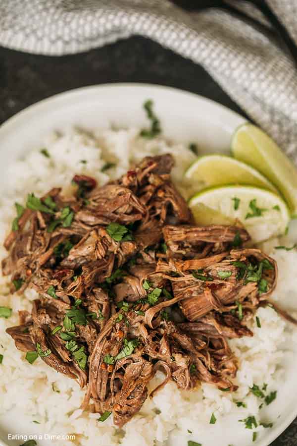 Close up image of Barbacoa Beef over rice topped with cilantro and a side of limes. 