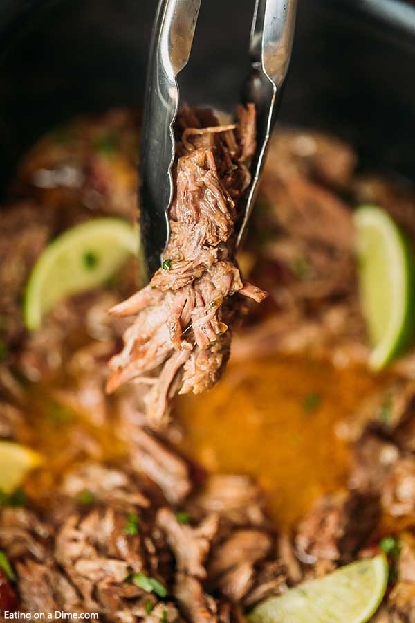 Close up image of Barbacoa Beef in the crock pot with a serving on a kitchen utensil. 