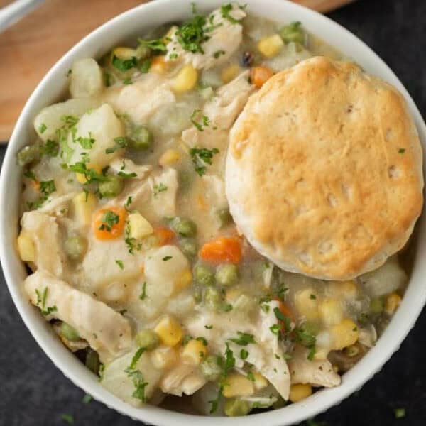 A bowl of creamy Instant Pot Chicken Pot Pie filling with peas, carrots, corn, and potatoes, topped with a golden-brown biscuit and sprinkled with chopped parsley.