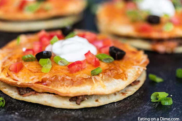 close up image of mexican pizza sliced and topped with sour cream. 