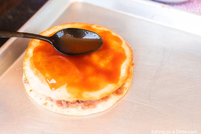 Close up image of Mexican Pizza on a cookie sheet being topped with enchilada sauce. 