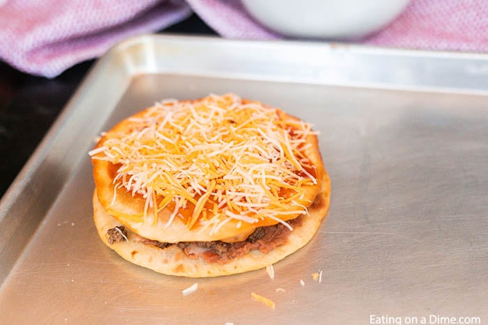 Topping the Mexican Pizza with shredded cheese on a baking sheet