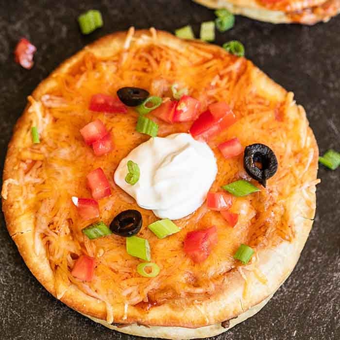 close up image of mexican pizza sliced and topped with sour cream. 