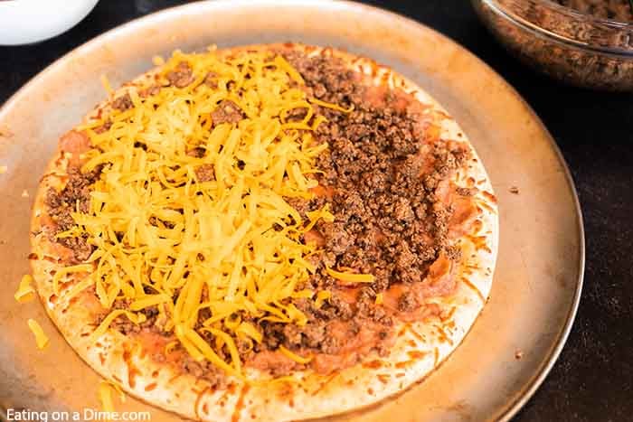 Our family loves this Taco pizza recipe with pizza crust and it is so easy to prepare. This easy homemade Mexican pizza with refried beans is loaded with so much flavor and tons of delicious toppings. #eatingonadime #tacopizzarecipe