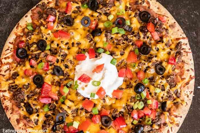 Our family loves this Taco pizza recipe with pizza crust and it is so easy to prepare. This easy homemade Mexican pizza with refried beans is loaded with so much flavor and tons of delicious toppings. #eatingonadime #tacopizzarecipe