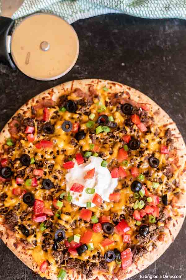 Our family loves this Taco pizza recipe with pizza crust and it is so easy to prepare. This easy homemade Mexican pizza with refried beans is loaded with so much flavor and tons of delicious toppings. #eatingonadime #tacopizzarecipe