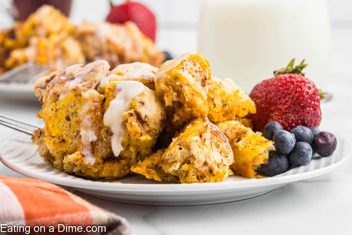 A serving of Pumpkin Cinnamon Roll Casserole on a plate with a side of fresh strawberries and blueberries.