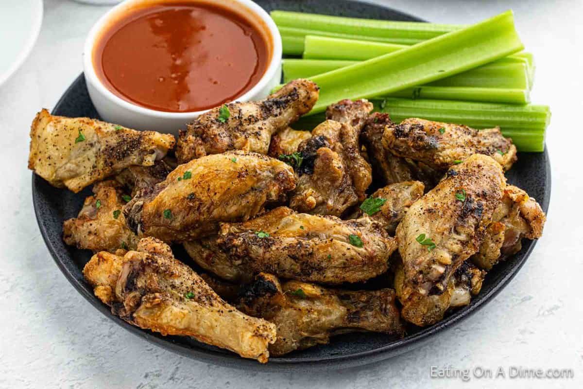 Air Fryer Chicken Wings stacked on a plate with a celery sticks and a bowl of red sauce on the side.