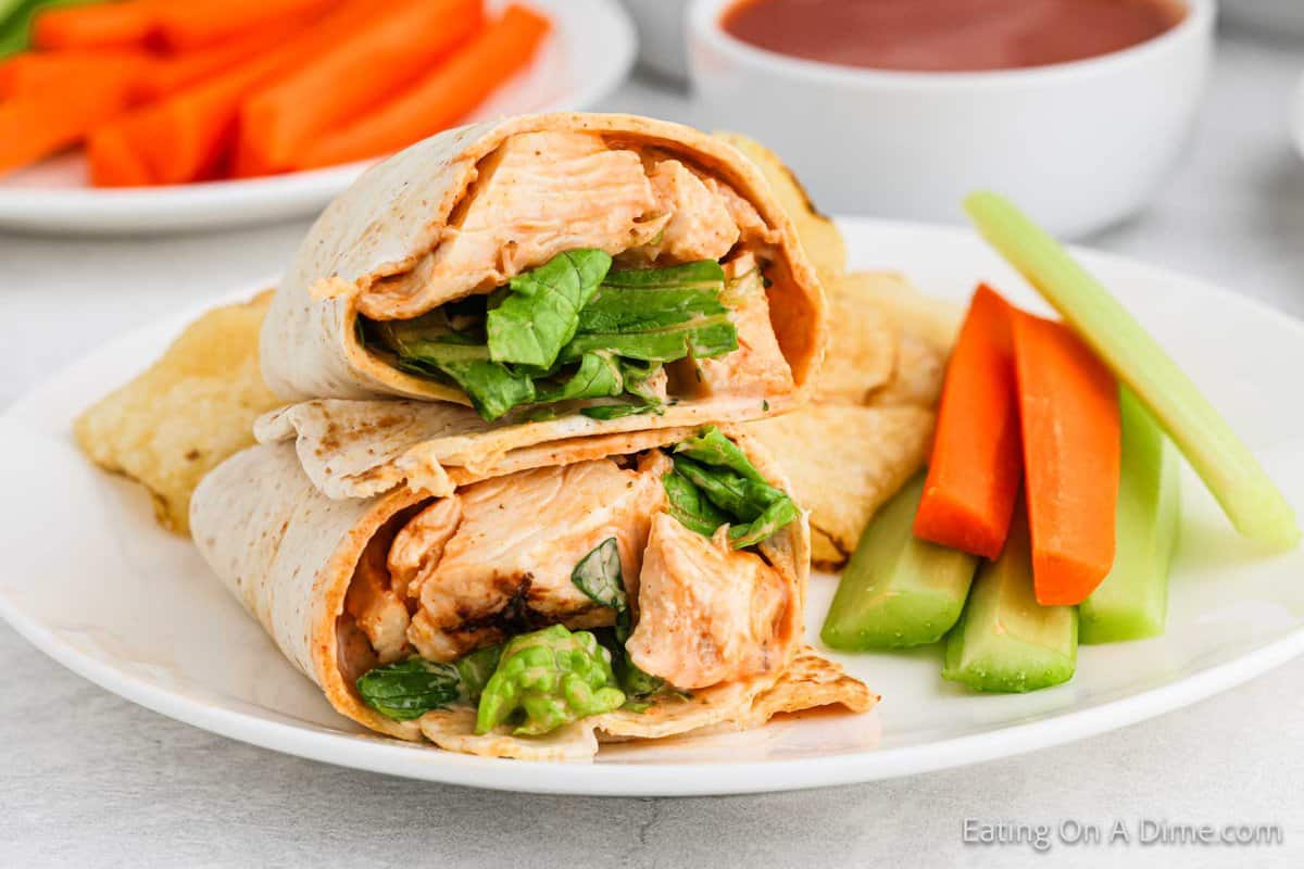 Buffalo Chicken Wrap cut in half stacked on a plate with a side of fresh carrot sticks and celery sticks.