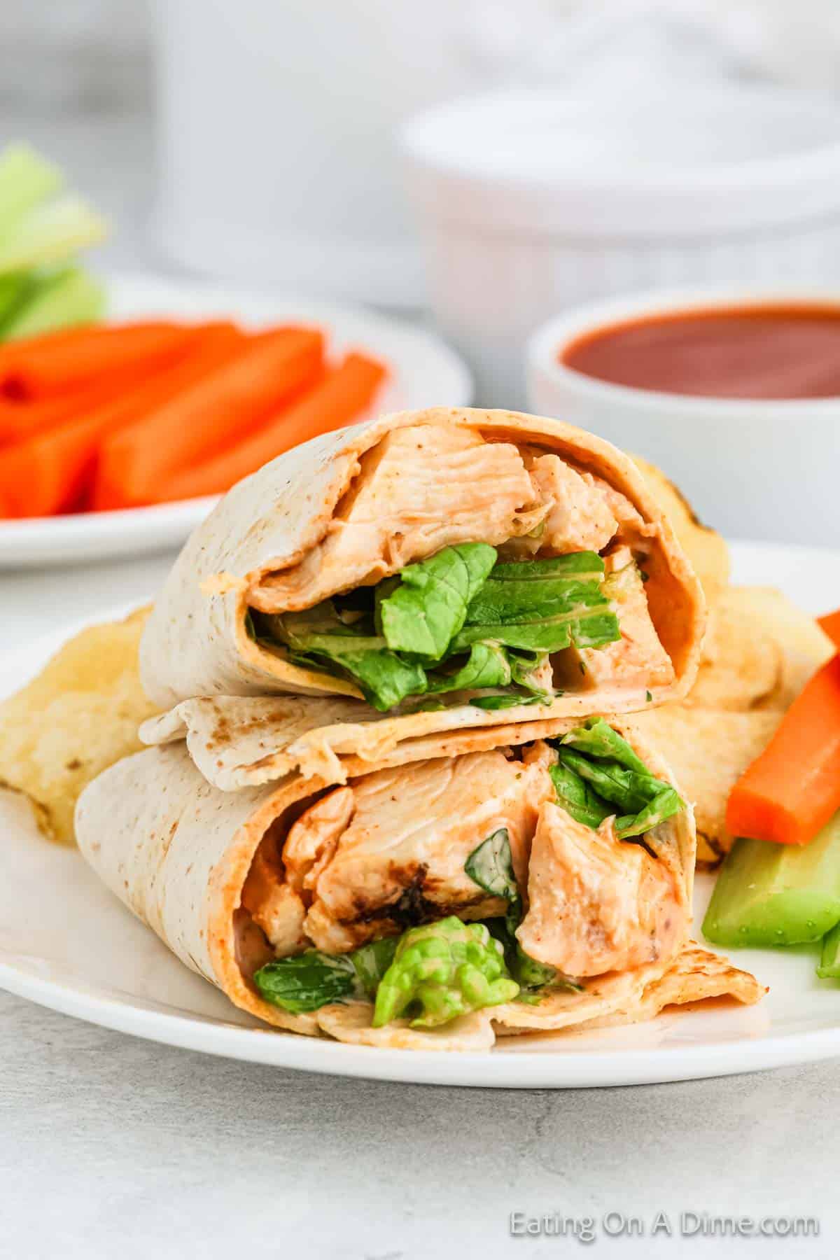 Buffalo Chicken Wraps cut in half on a plate with celery and carrots and a side of potato chips