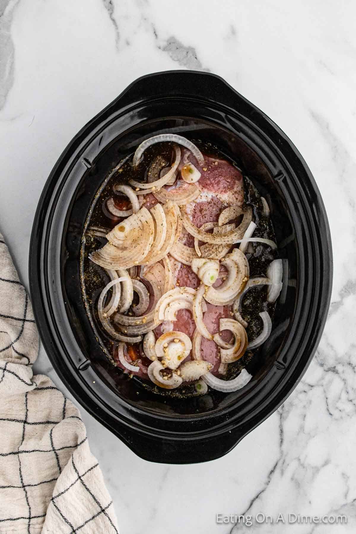 Pouring the sauce over the pork loin and onions in the slow cooker