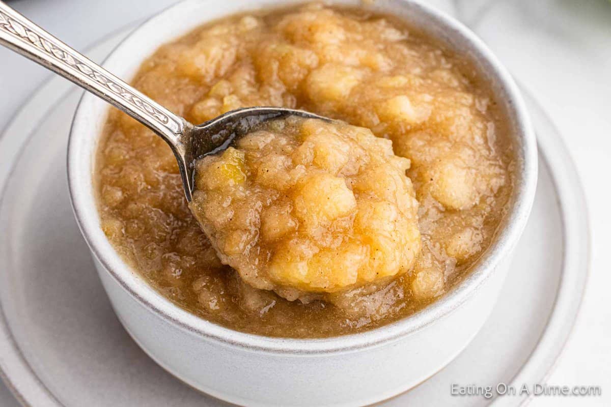 Close up image of applesauce in a white bowl with a bite on the spoon