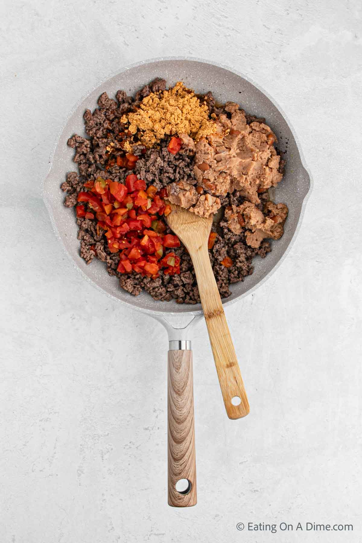 Combining the ground beef mixture in a skillet with a wooden spoon