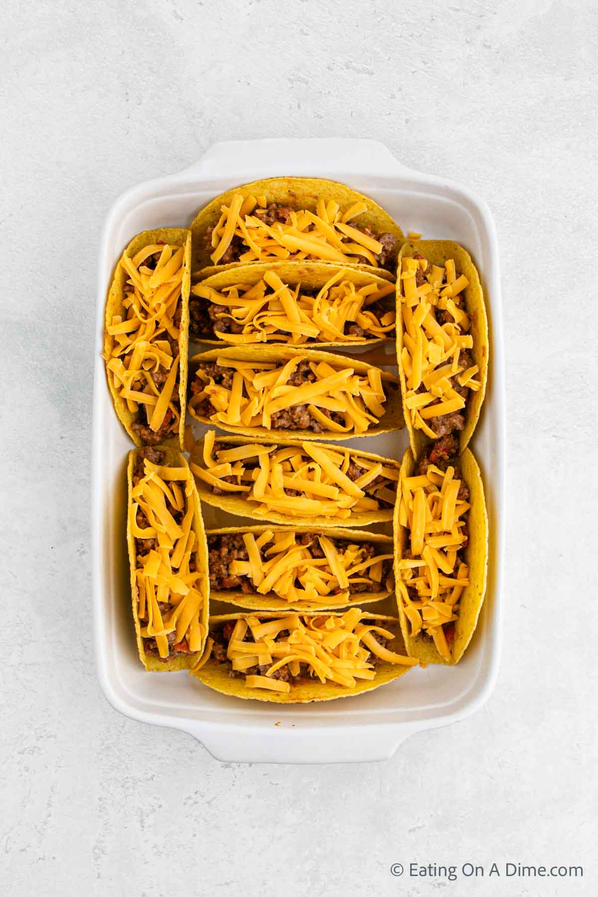 Topping the ground beef with shredded cheese in a baking dish