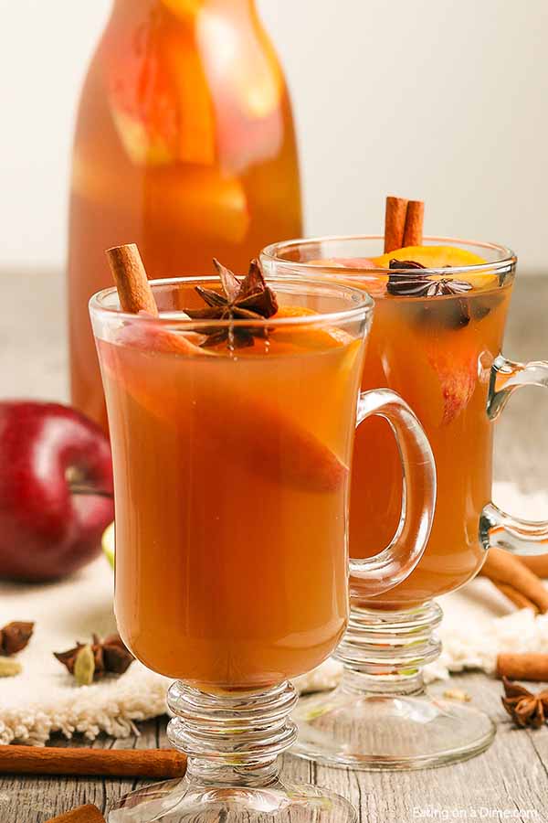 Apple Cider in clear mugs topped with cinnamon sticks and fresh apples and oranges