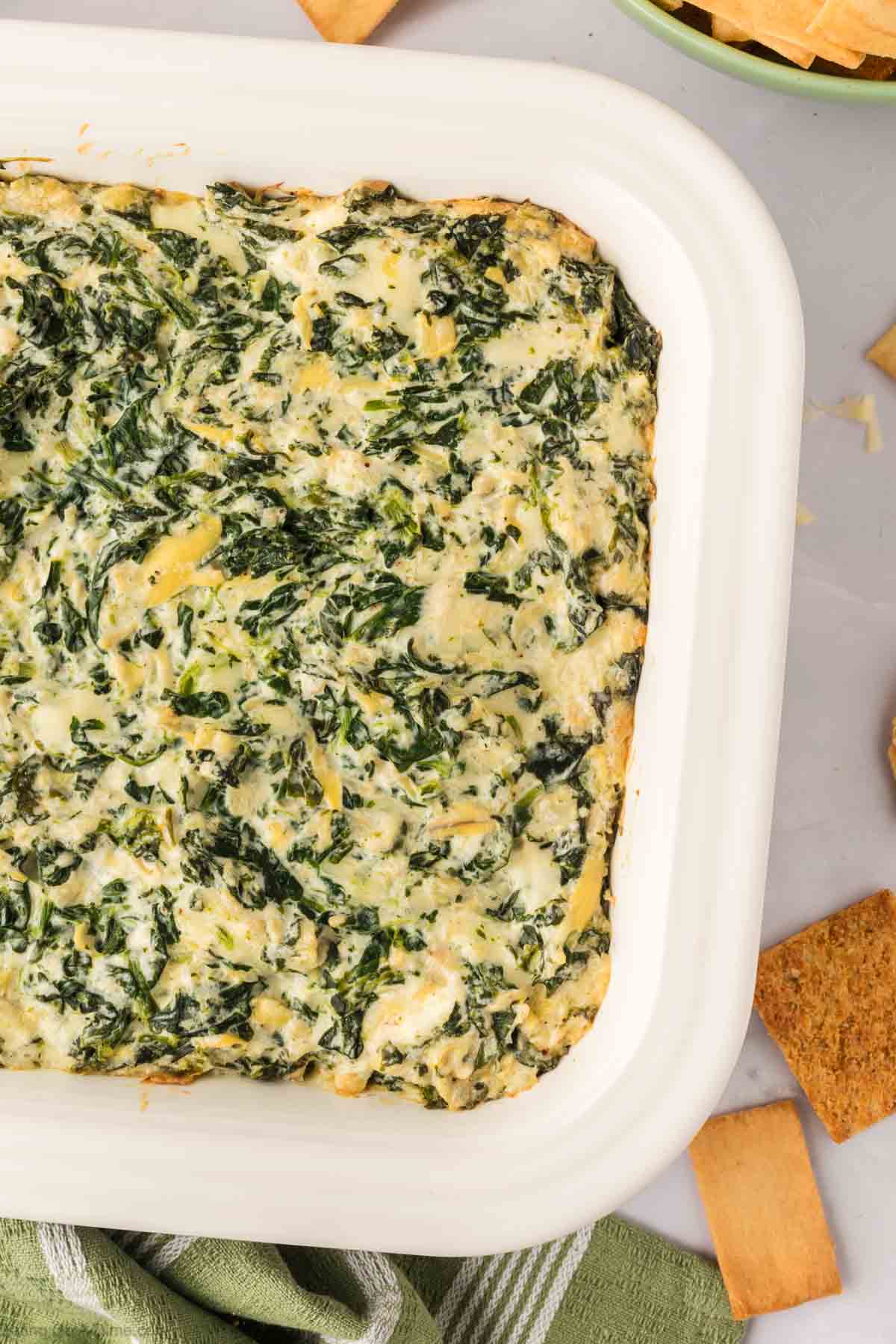 Spinach Artichoke Dip in a white casserole dish with a side of slice bread and chips
