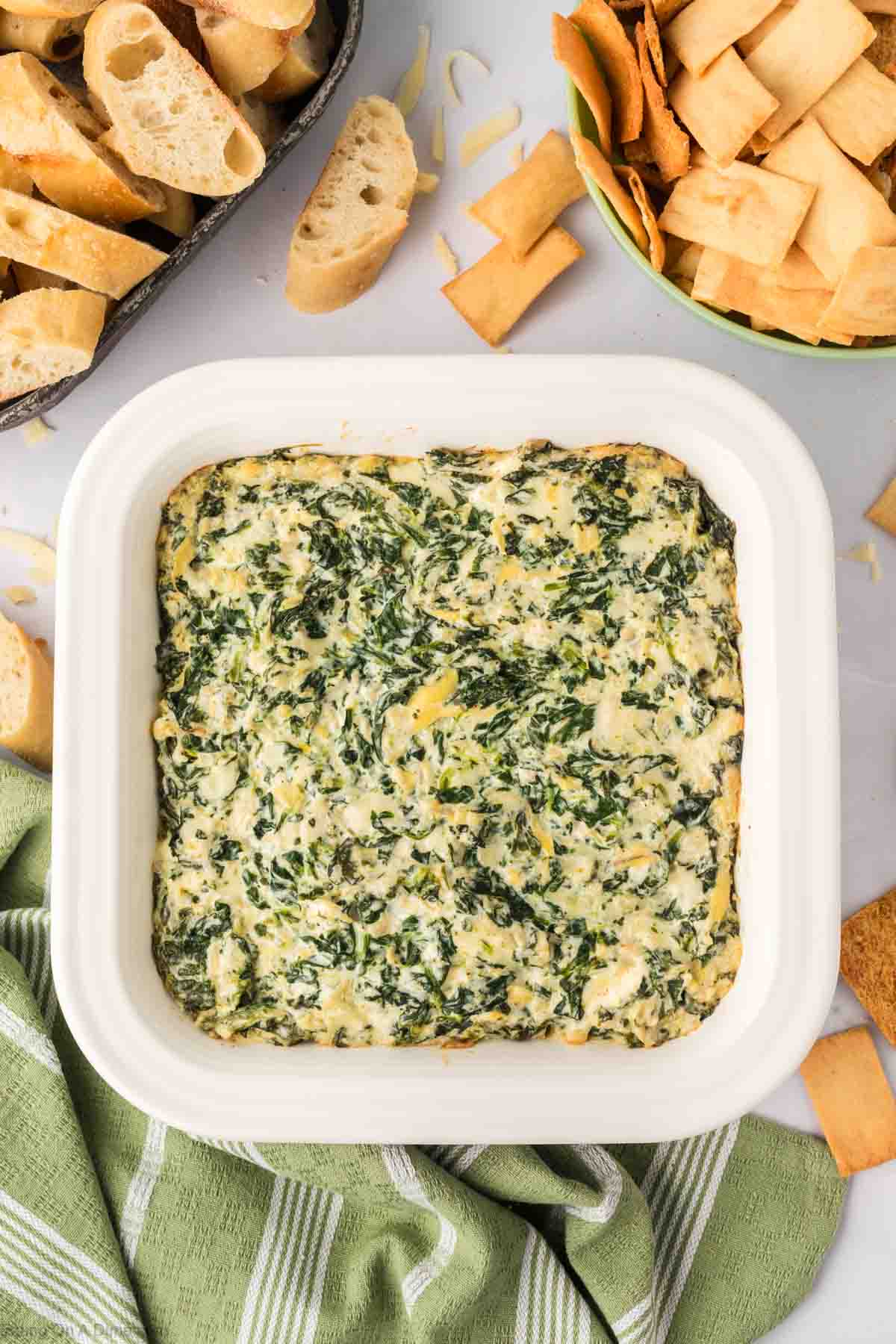 Spinach Artichoke Dip in a white casserole dish with a side of slice bread and chips