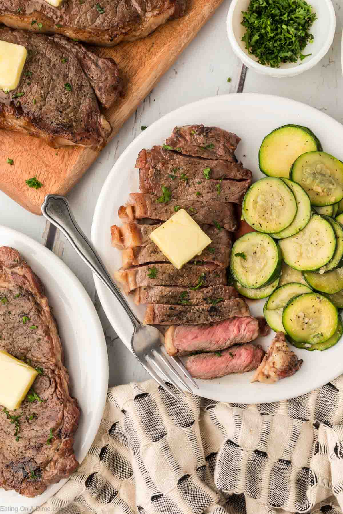 Grilled Steak on a plate topped with a slice of butter and a side of slice zucchini