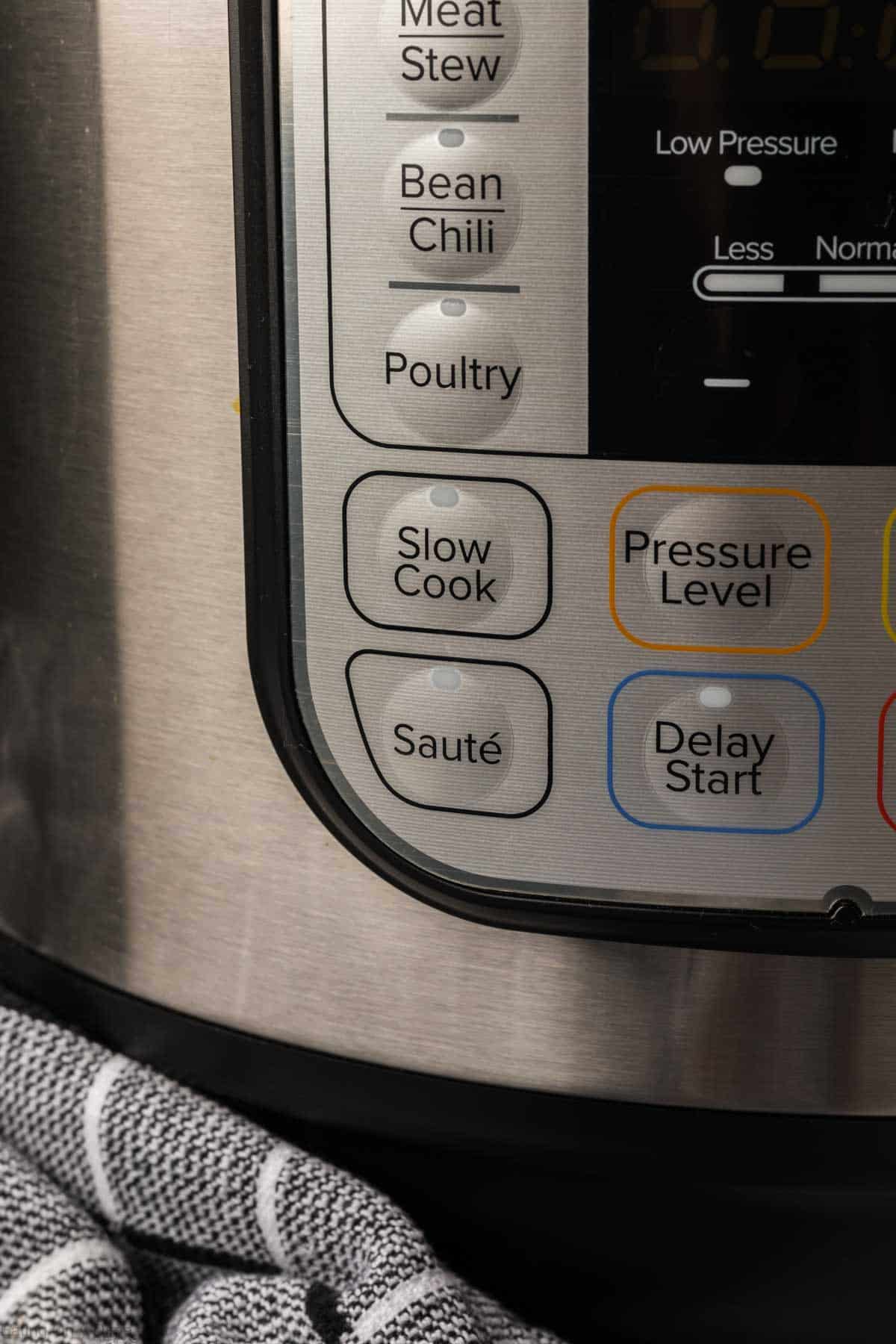 Close-up of an Instant Pot control panel with Sauté, Slow Cook, Poultry, Bean Chili, Meat Stew, Pressure Level, and Delay Start buttons—perfect for making Instant Pot Pork Chops with Gravy—plus a striped kitchen towel in the foreground.