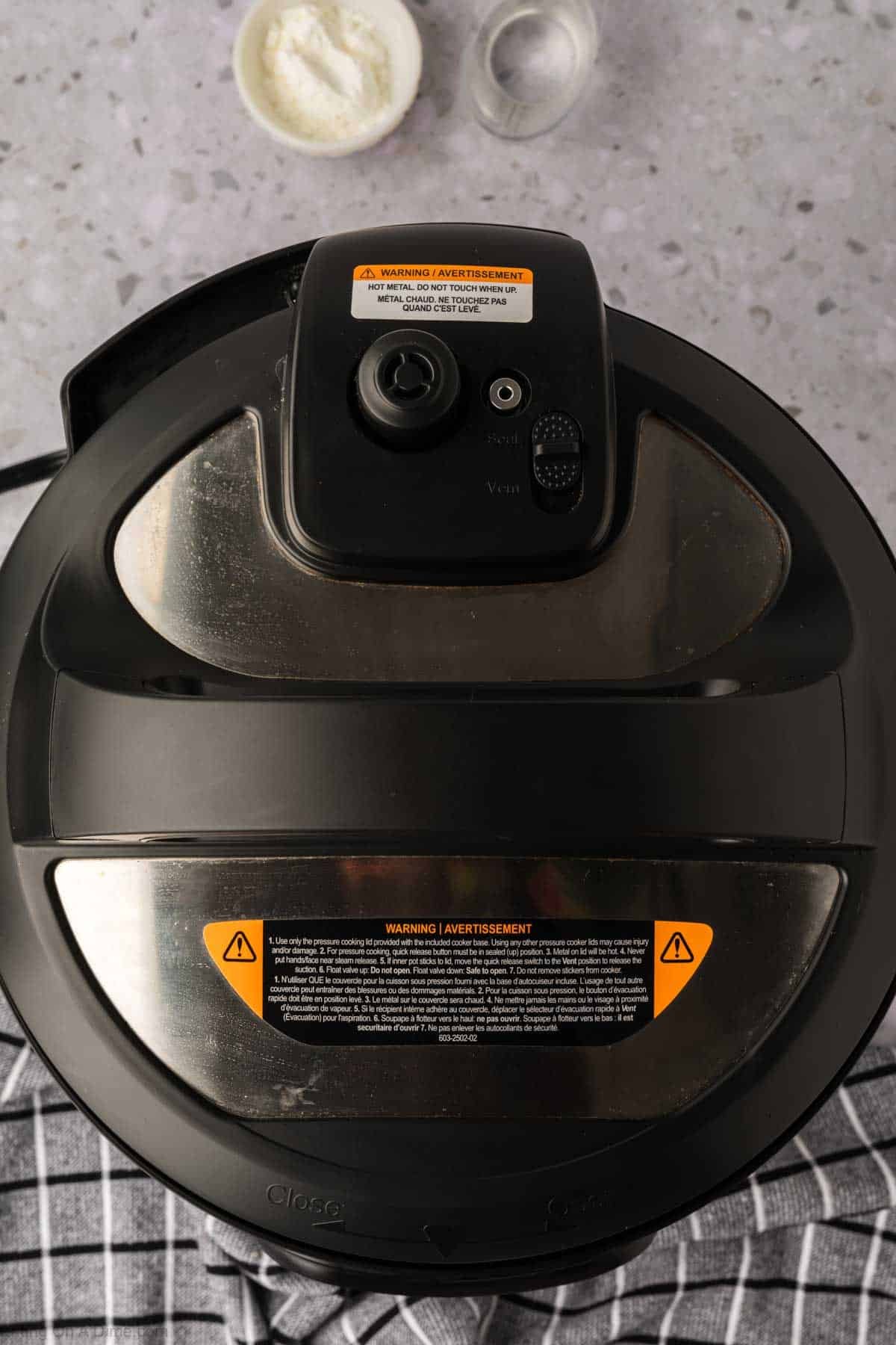 Top-down view of a closed Instant Pot on a striped towel, with a bowl of salt and another of flour nearby—perfect setup for making Instant Pot Pork Chops with Gravy on a speckled countertop.