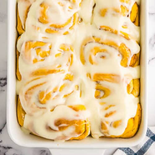 Pumpkin cinnamon rolls in white and yellow hues are served in a white dish.