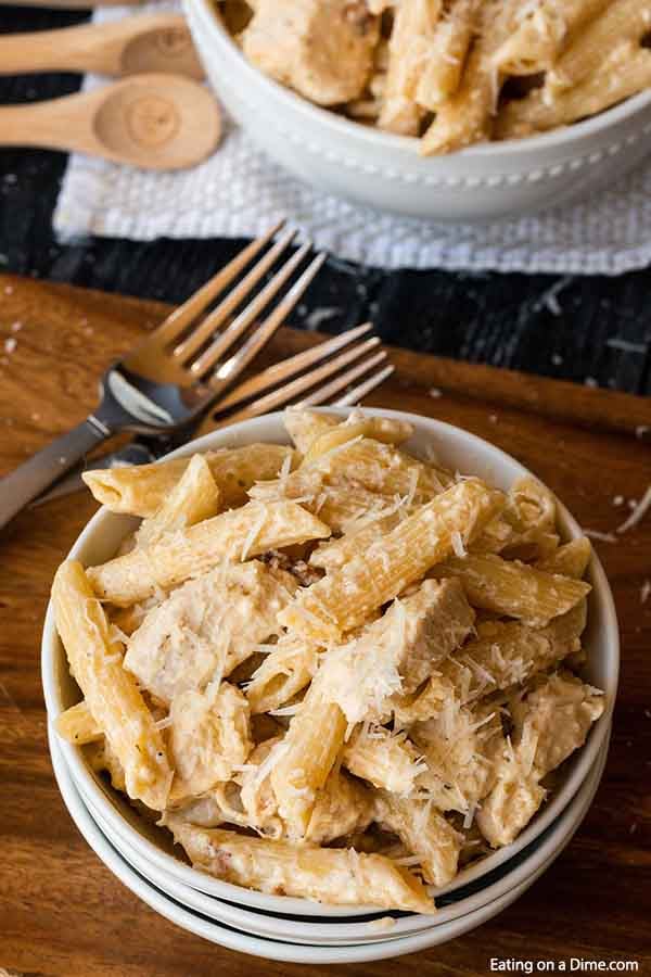 A white bowl full of this Crock Pot Olive Garden Chicken Alfredo Pasta on a wooden board with 2 forks next to it. 